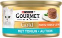 Blikje Gourmet Gold Hartig Torentje met Tonijn kattenvoer. Een witte kat kijkt naar de camera, naast een portie van het voer op een schoteltje.