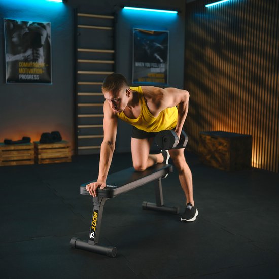 Man met gele tanktop doet dumbbell row op zwarte trainingsbank.