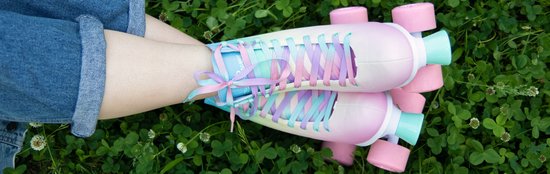 Geknoopte paarse, roze en blauwe veters op pastelkleurige roller skates, gedragen met een spijkerbroek op een grasveld.