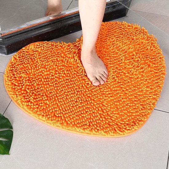 Oranje hartvormige badkamermat met pluizige textuur. Een voet staat erop.