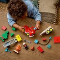 Un jeune enfant construit avec des briques LEGO Duplo rouges et vertes, dont un camion de pompiers et un pompier.