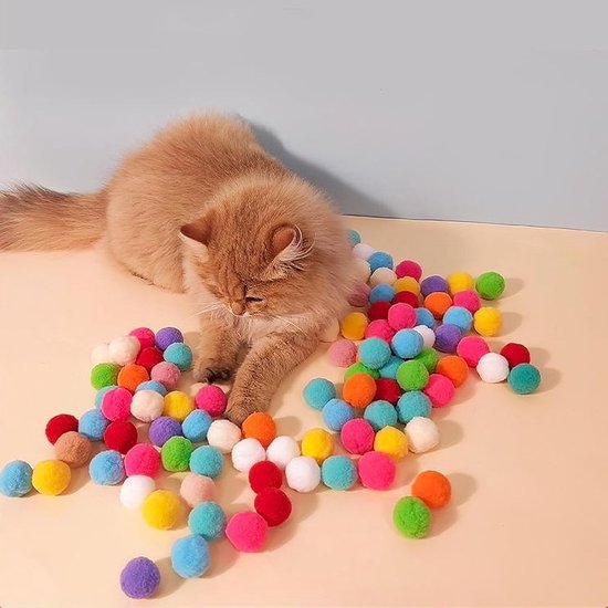 Een kat ligt tussen veel felgekleurde pomponballetjes.