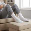 Man in grijze pyjamabroek en witte Hipperboo sokken zit op een stoel met een kopje.