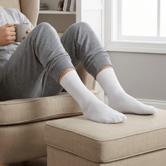 Man in grijze pyjamabroek en witte Hipperboo sokken zit op een stoel met een kopje.