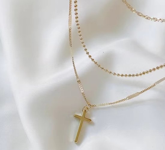 Gouden gelaagde ketting met kruishanger op witte satijnen stof.