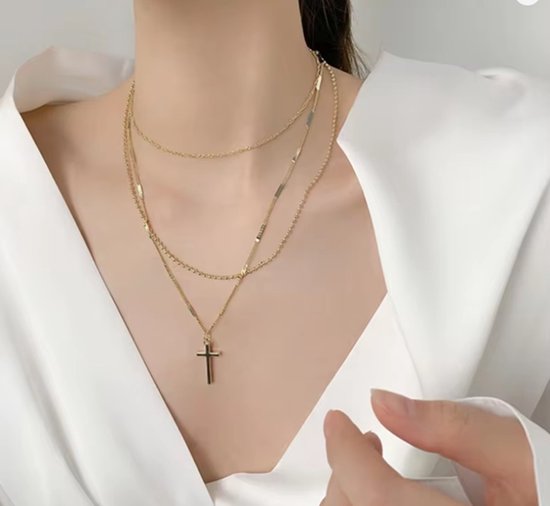 Model draagt een gouden gelaagde ketting met kruishanger onder een witte blouse.