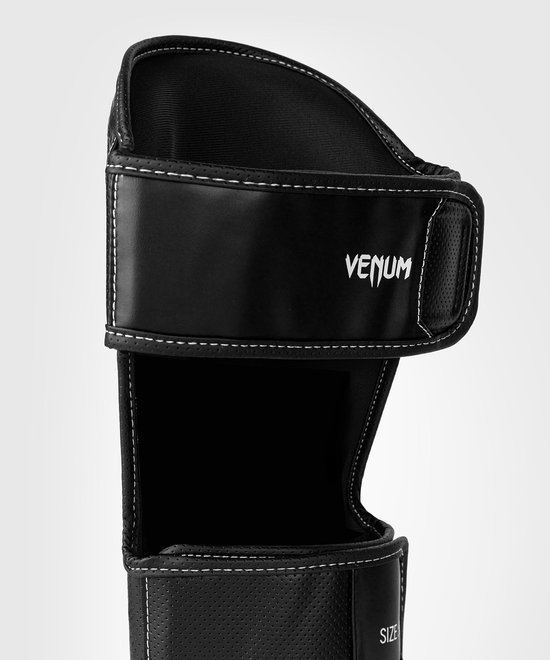 Detail van zwarte scheenbeschermer met klittenbandsluiting, Venum logo en perforaties.