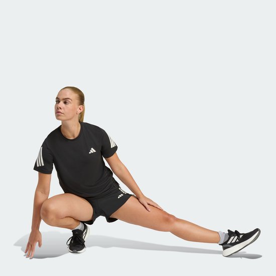 Vrouw in zwart sportshirt en -short met witte Adidas strepen, stretcht.