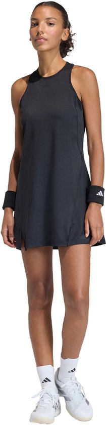 Femme portant une robe de tennis noire sans manches avec fentes, chaussettes et chaussures blanches.