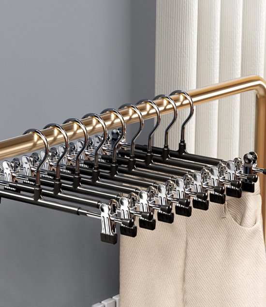 Rij van zilveren kledinghangers met zwarte clips die beige broeken ophangen aan een gouden rail.