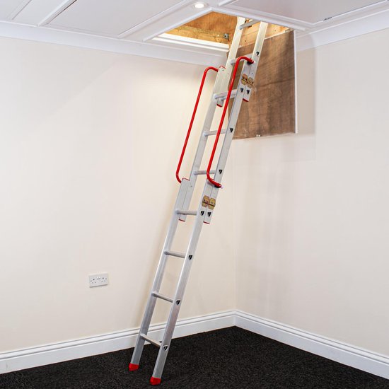Aluminium lofttrap met rode dubbele leuningen die uit een zolderluik in een wit plafond komen, met een donkere vloer.