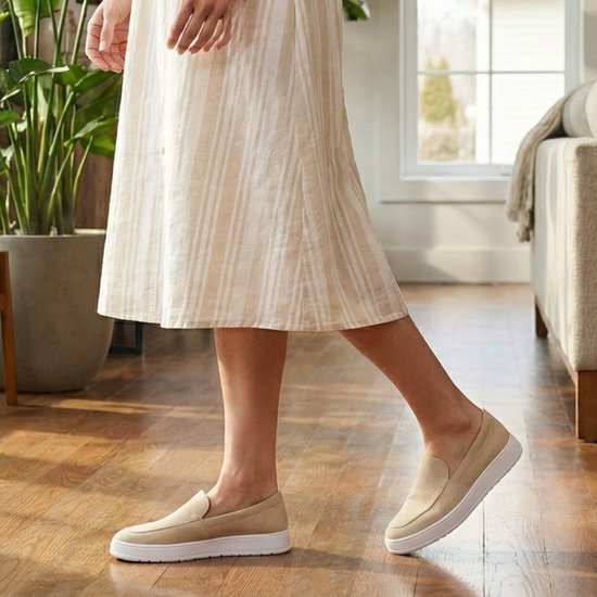 Persoon in gestreepte jurk draagt beige instappers met witte zolen.