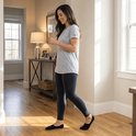 Een vrouw loopt in een woonkamer, draagt een grijze T-shirt, donkere legging en zwarte SUKATS invisible sokken.
