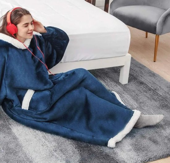 Een vrouw in een donkerblauwe oversized hoodie met witte fleece voering en rode koptelefoon zit op een vloerkleed.