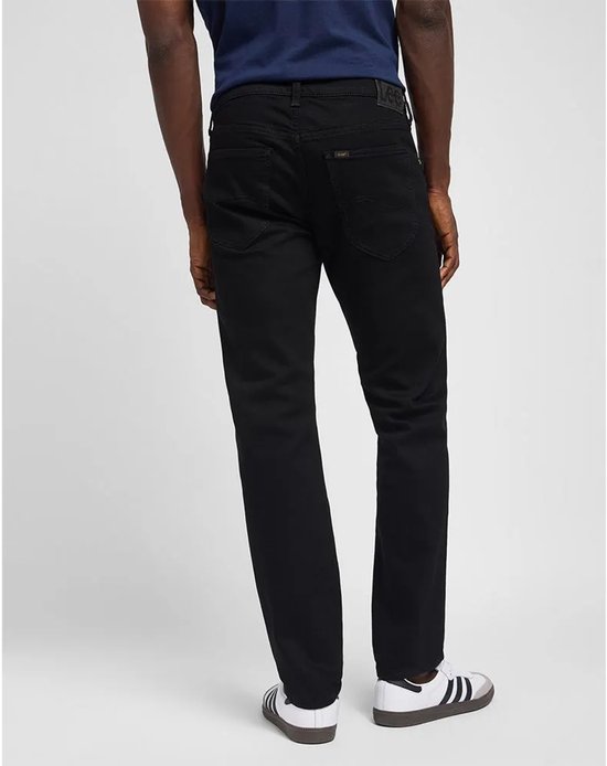 Man in donkerblauwe top en zwarte jeans, zicht van achteren. Draagt witte sneakers met strepen.