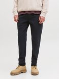 Man draagt een donkerblauwe joggingbroek met naden, beige hoodie en bruine boots.