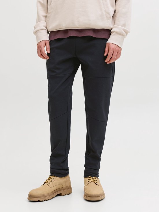 Man draagt een donkerblauwe joggingbroek met naden, beige hoodie en bruine boots.