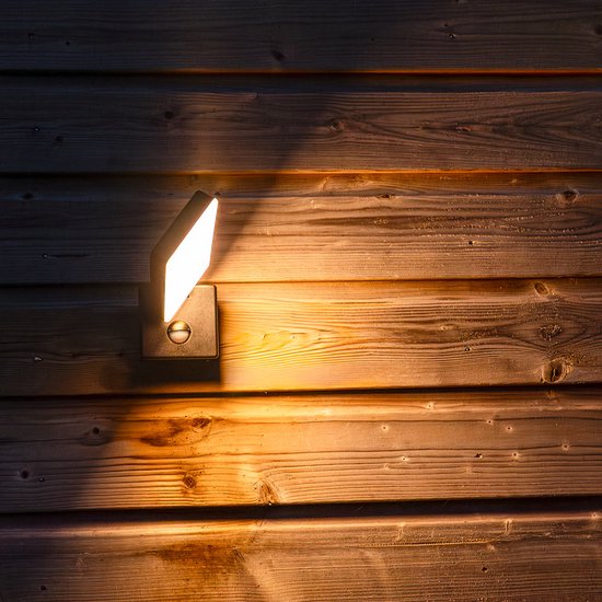 Zwarte wandlamp met sensor, verlicht de houten schutting met geel licht.