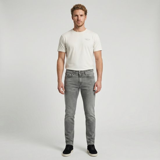 Man met grijze slim fit jeans en een beige T-shirt. De jeans heeft een normale pasvorm.