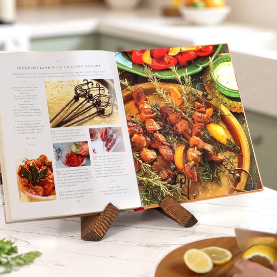 Een houten boekenstandaard houdt een kookboek open, met een recept voor "SKEWERED LAMB WITH CILANTRO YOGURT" en een grote foto van het gerecht.