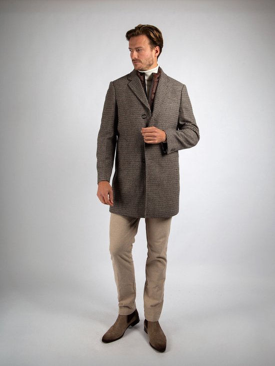 Man in een bruin-beige pied-de-poule jas, beige broek en bruine suède schoenen.
