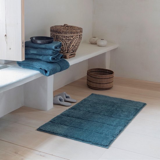 Antracietkleurige badmat met horizontale banen, in een badkamer met blauwe handdoeken.
