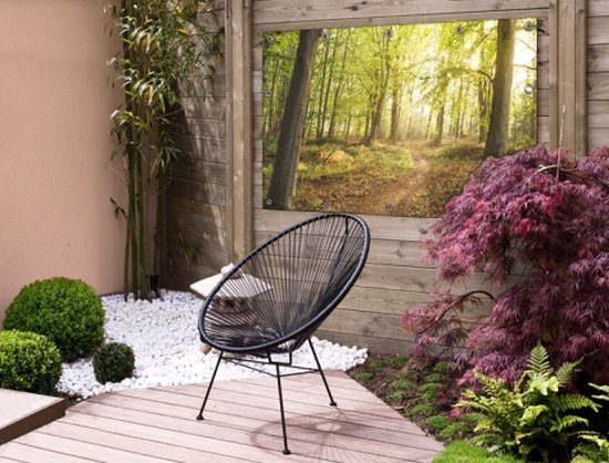 Een tuinposter van een bos met een pad in een moderne tuin met een zwarte stoel.