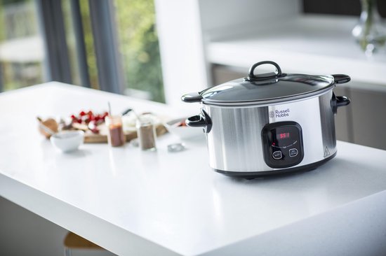 Zilverkleurige Russell Hobbs slowcooker op een wit aanrecht met ingrediënten op de achtergrond.