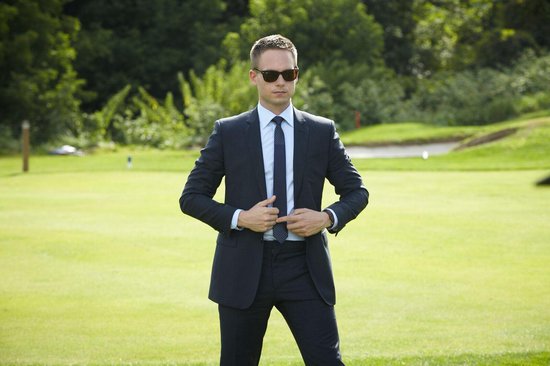 Man in donkergrijs pak met zonnebril, staand op een golfbaan.
