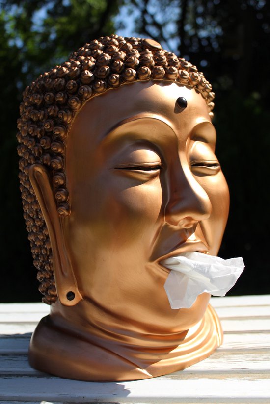 Gouden Boeddha hoofd met witte tissue uit de mond, zittend op een witte tafel.