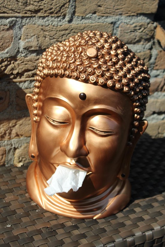 Gouden Boeddha hoofd met tissue uit de mond, buiten op een bruine tafel.