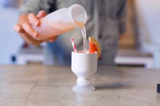 Witte Dopper fles wordt leeggeschonken in een bijpassende witte beker met grapefruit en rietje.