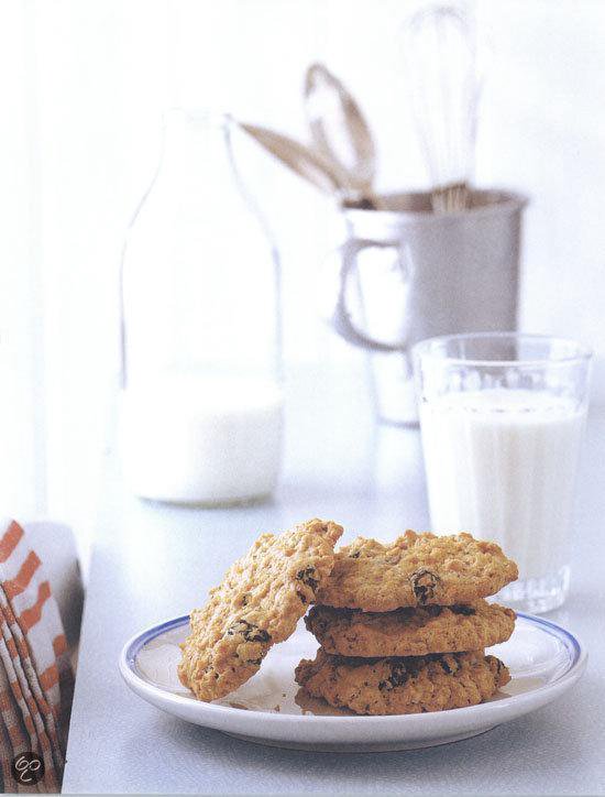 Stapel koekjes met rozijnen op een wit bord met blauwe rand, naast een glas melk.