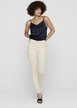 Model met een navy top en beige skinny jeans, gezien vanaf de voorkant.