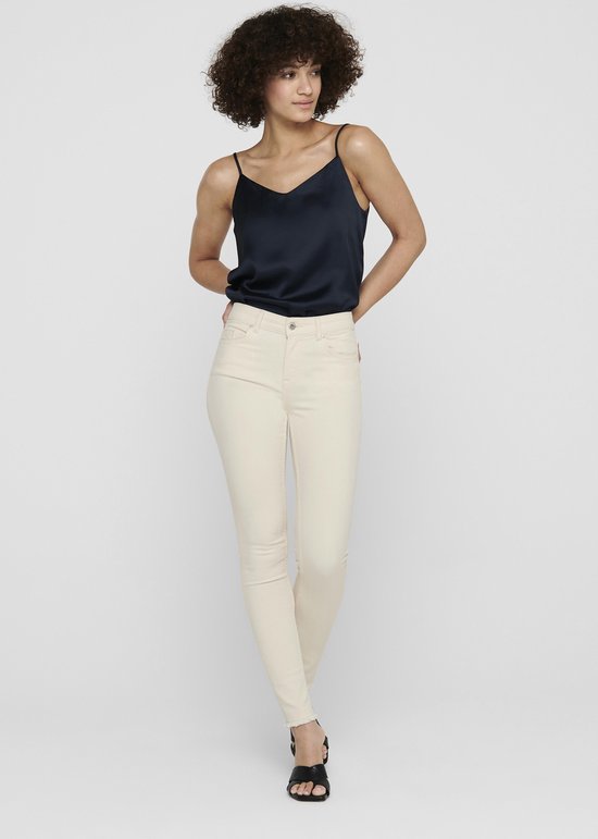 Model met een navy top en beige skinny jeans, gezien vanaf de voorkant.