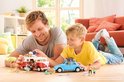 Vader en zoon spelen met een PLAYMOBIL camperbus en een blauwe kever, met toebehoren.