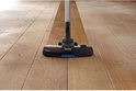 Brosse d'aspiration noire avec accents bleus nettoie un plancher en bois.