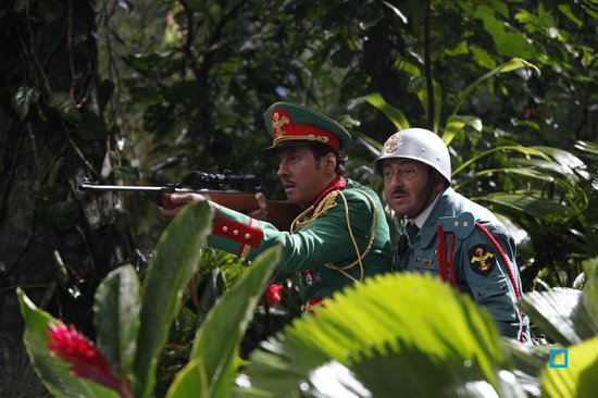 Twee mannen in militaire uniformen in een jungle, één richt een geweer.