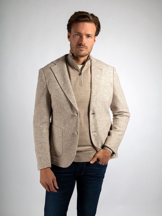 Man in beige colbert met kleine ruitjes, beige trui met rits en spijkerbroek.