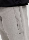 Close-up van een grijze joggingbroek met een ritsvak en 'JJ Athletic Dept.' opdruk.