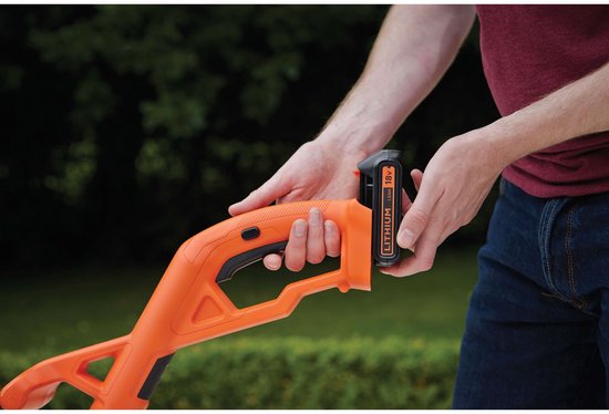 Een man verwisselt de 18V accu van de oranje grastrimmer.