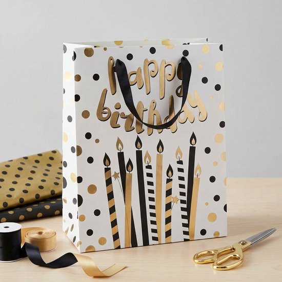 Sac cadeau blanc à pois dorés et noirs, avec des bougies dorées et noires et l'inscription 'Happy Birthday'.