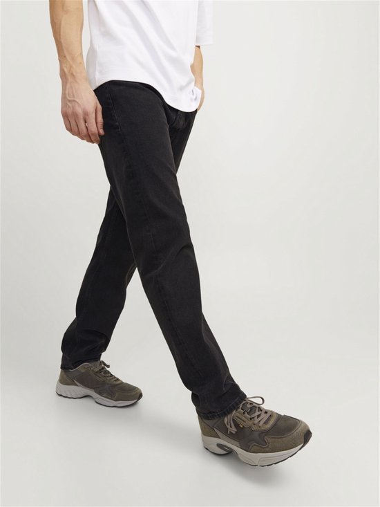 Man die loopt in losse zwarte jeans en grijze sneakers.