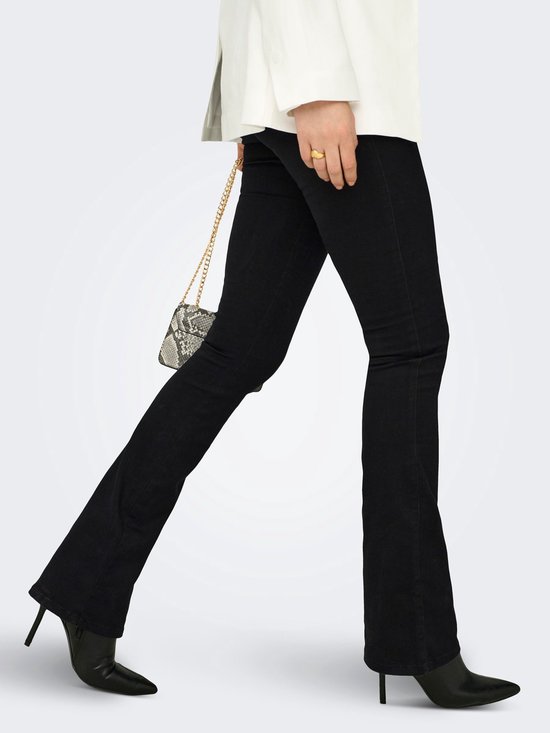 Model in zwarte flared jeans, witte blazer en zwarte laarzen.