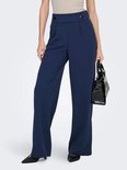 Model in marineblauwe wijde broek met hoge taille, twee knopen en een handtas.