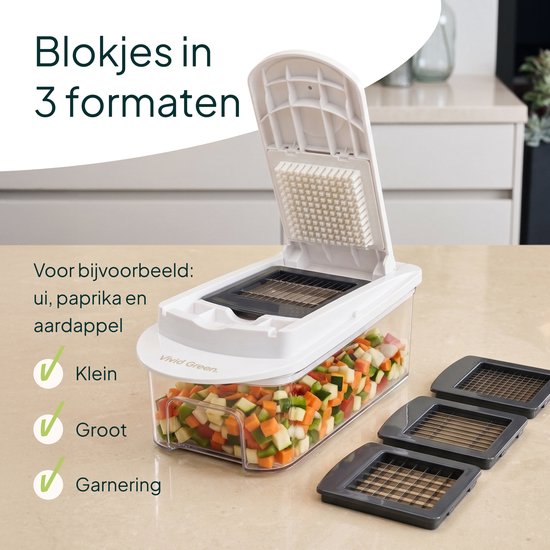 Witte groentesnijder met openklapbare deksel en een glazen bak vol blokjes gesneden paprika, wortel en courgette. Drie snij-inzetstukken ernaast.