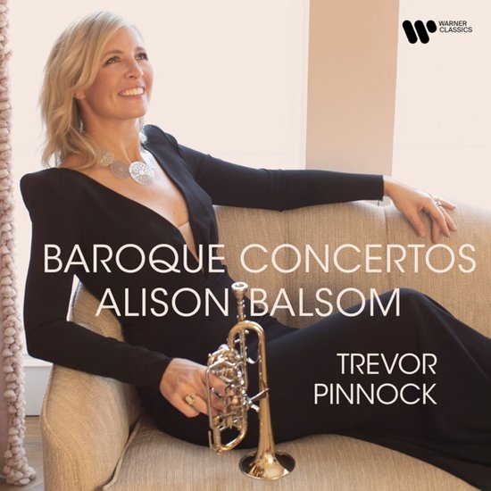 Alison Balsom in een zwarte jurk met een gouden trompet, zittend op een bank. "Baroque Concertos" met Alison Balsom, Trevor Pinnock, Warner Classics.