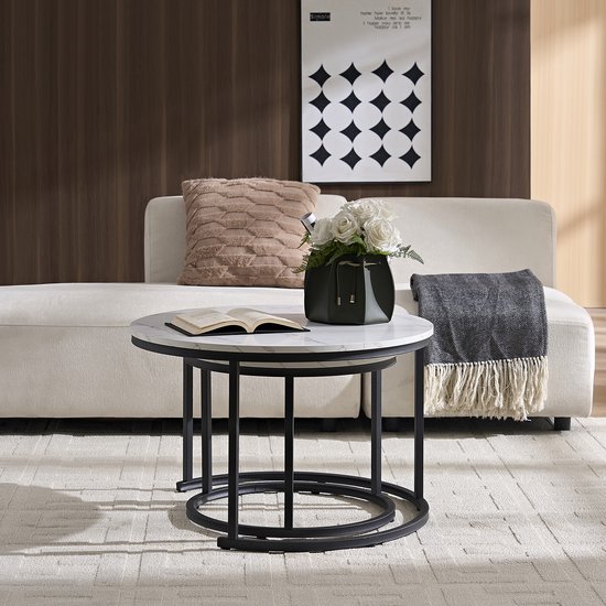 Twee ronde bijzettafels met marmerlook blad en zwart metalen onderstel. Eén tafel staat voor de bank, de ander er deels onder.