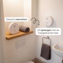 Wit, rond geluidshuisje met sensor op een houten plankje, naast een gevouwen handdoek.