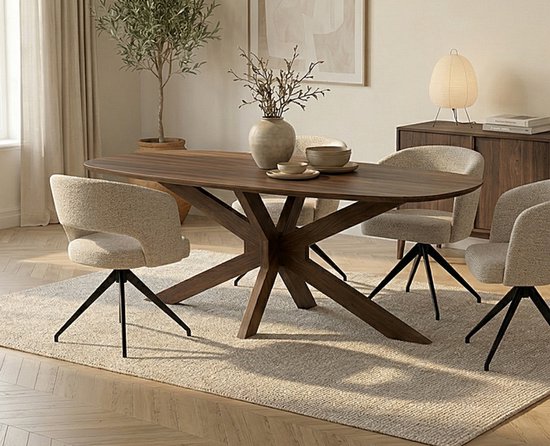 Eettafel Capricorn met een ovaal acaciahouten blad en een uniek houten onderstel, omringd door stoelen in een lichte stof.